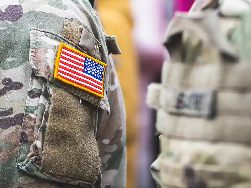 Close up of military person with a small American flag patched on their uniform sleeve, and another military person in the background but blurred out
